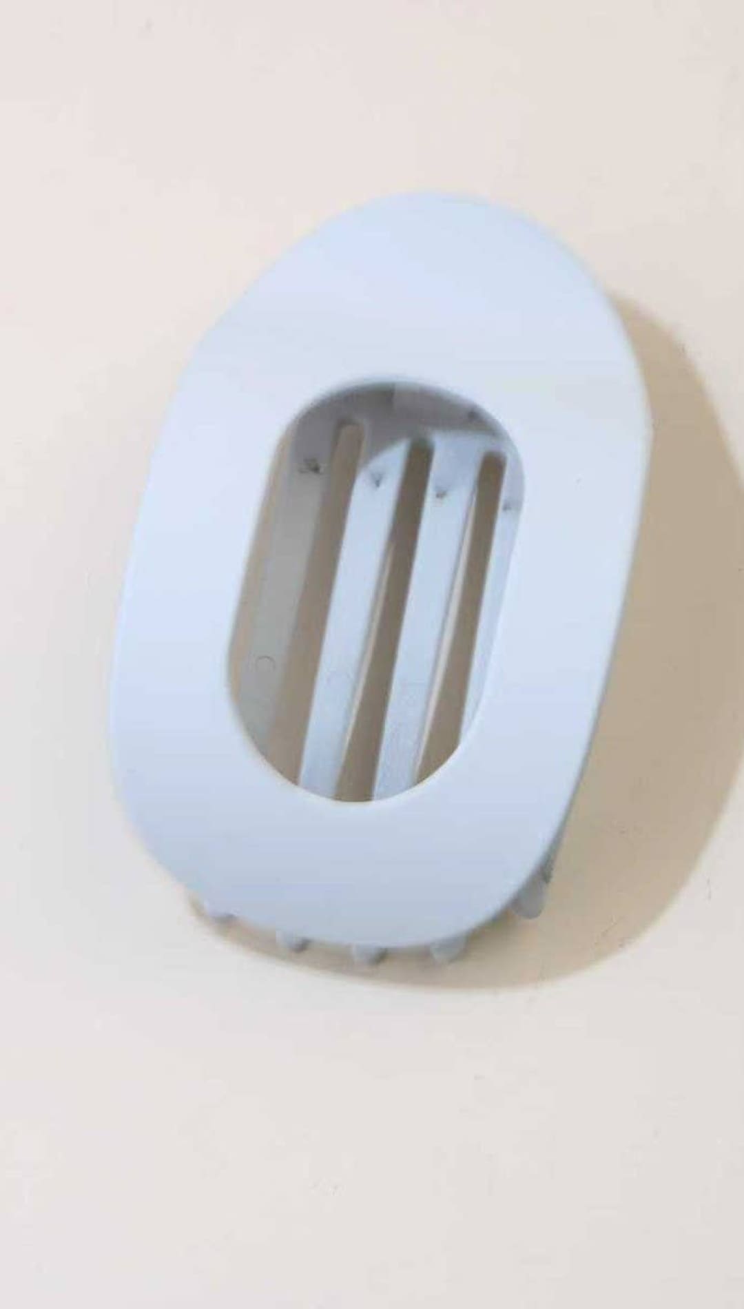 Pale blue oval-shaped plastic hair clip with vertical slits for grip.