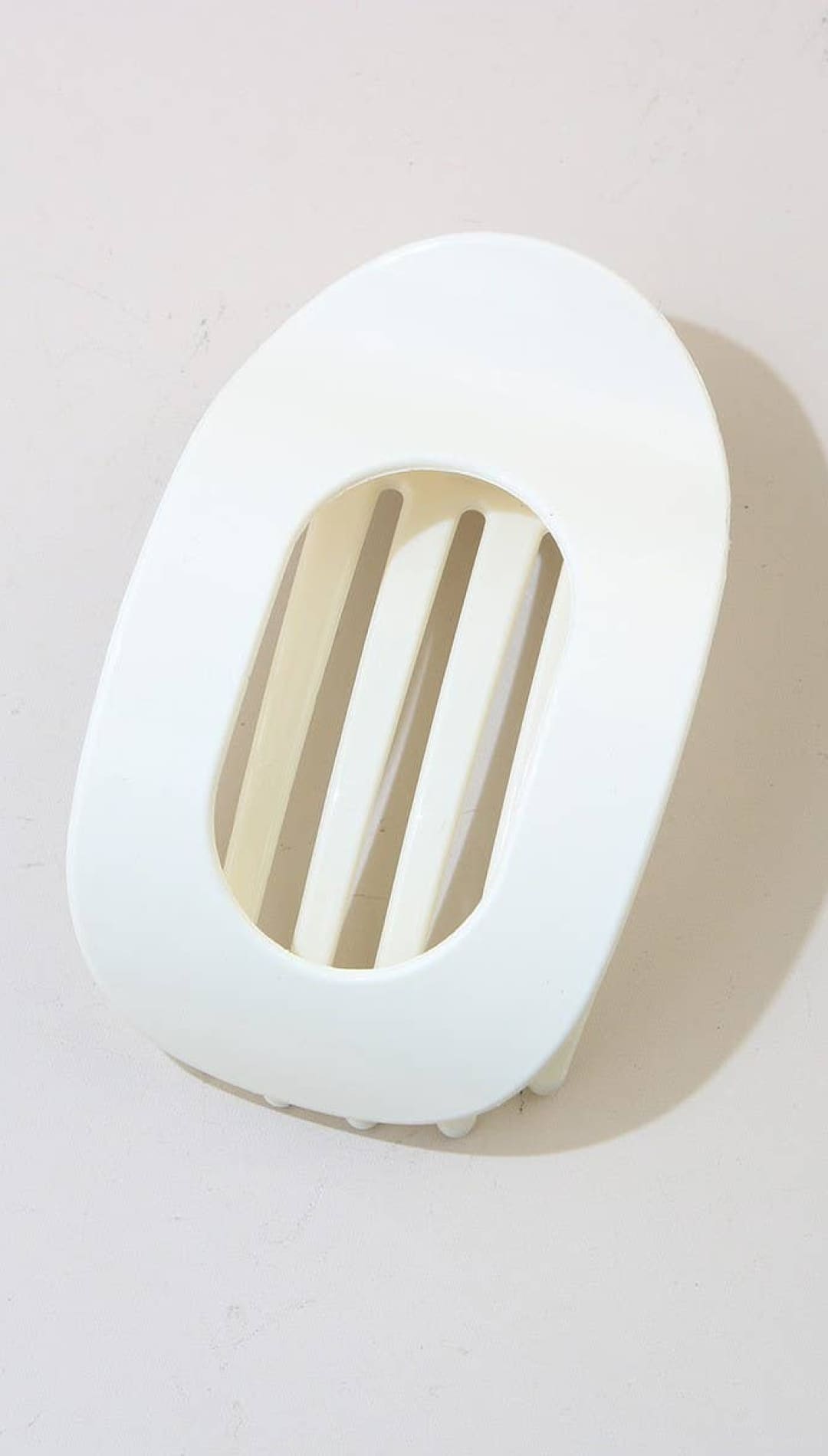 White oval-shaped soap dish with slats for drainage, likely made of ceramic or plastic.