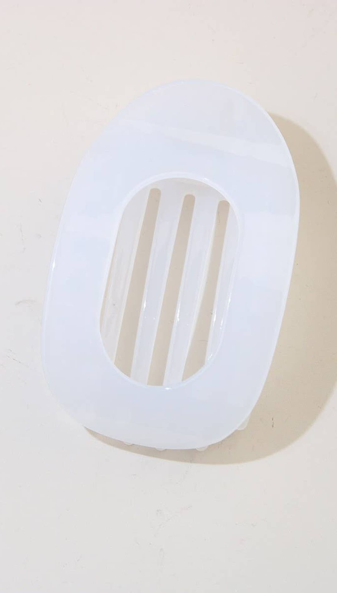 White oval soap dish with slits for drainage, made of plastic.