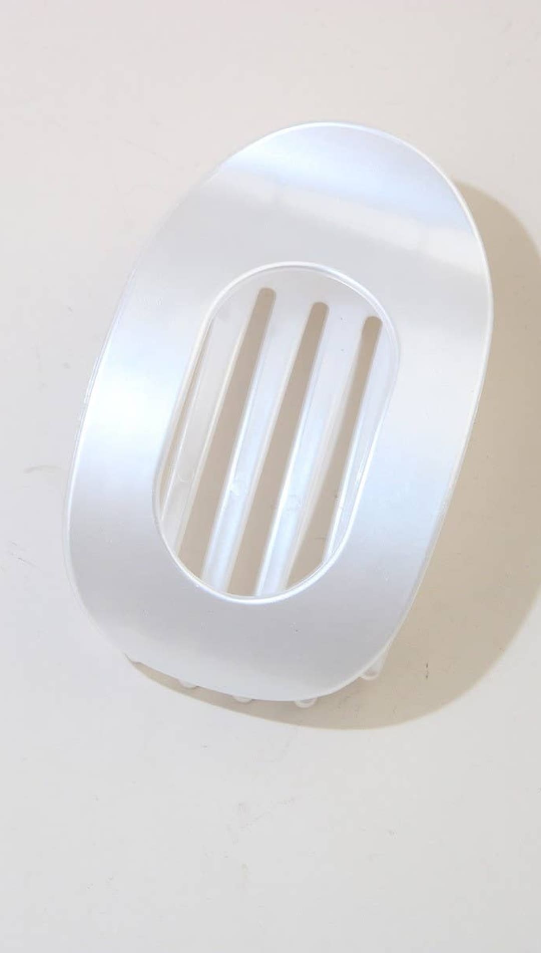 White oval soap dish with slits for drainage, made of plastic or ceramic.