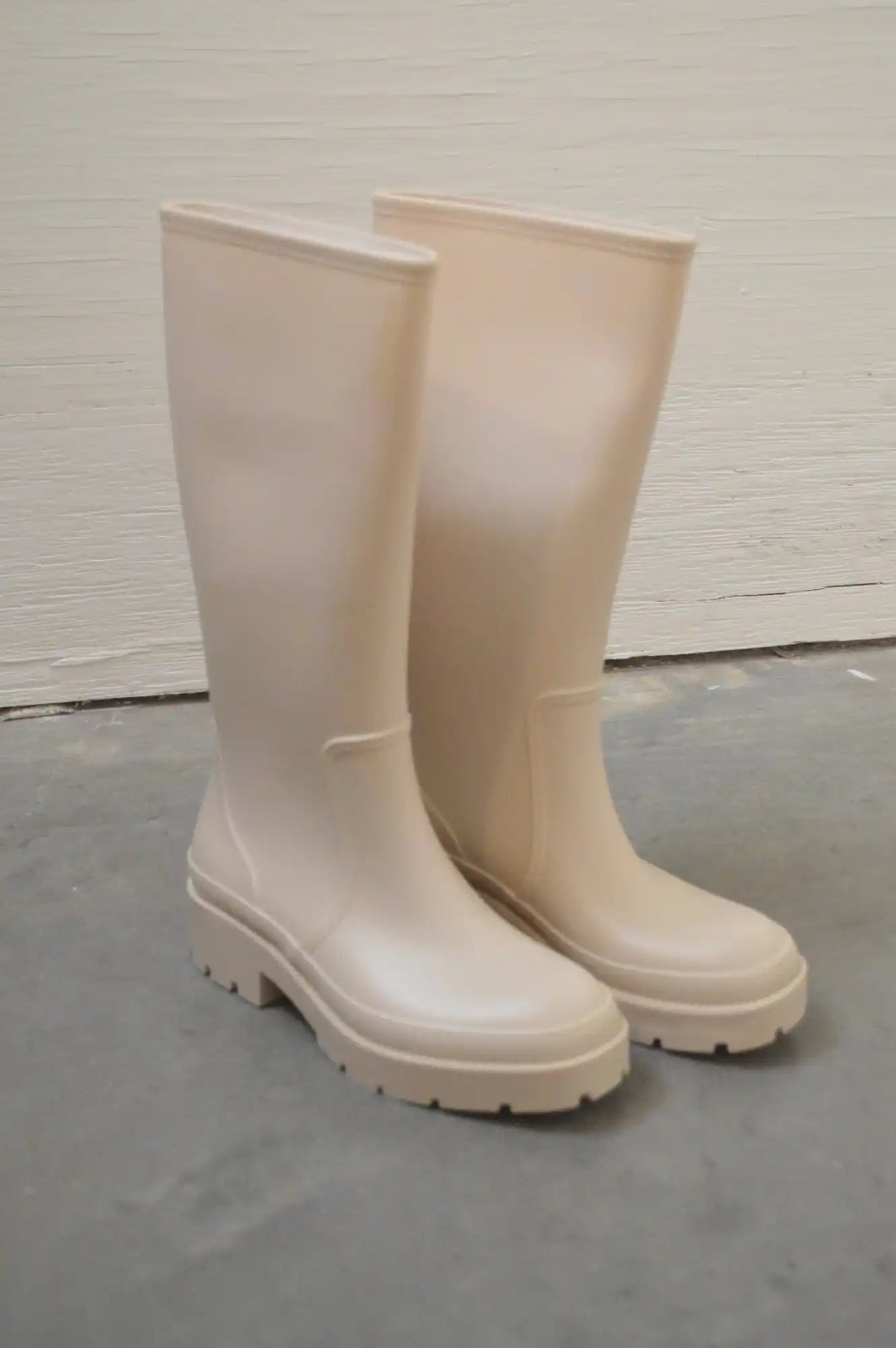 A pair of tall, light beige rubber rain boots with thick, lugged soles.