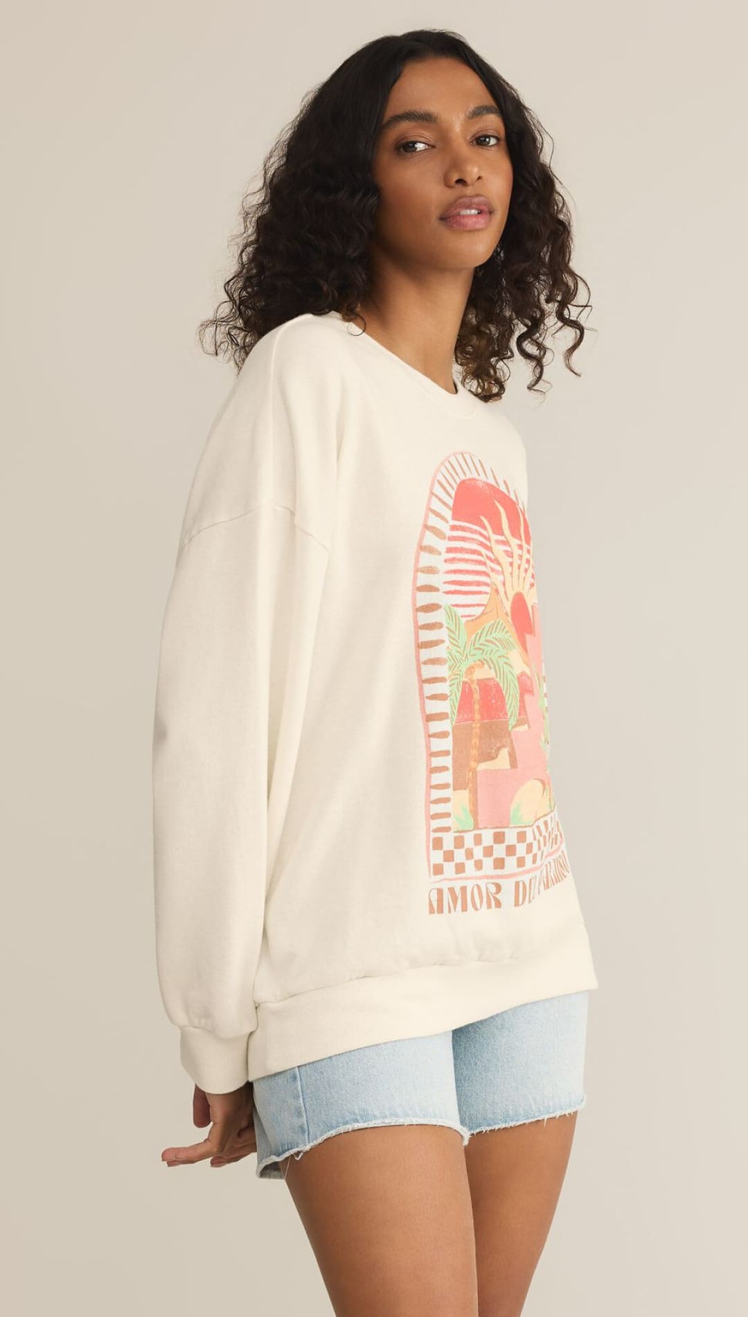 White sweatshirt with pink graphic design worn with denim shorts.