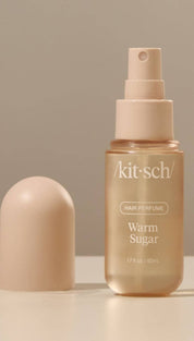 Beige spray bottle with gold accents and ’warm sugar’ label, likely made of plastic or glass.