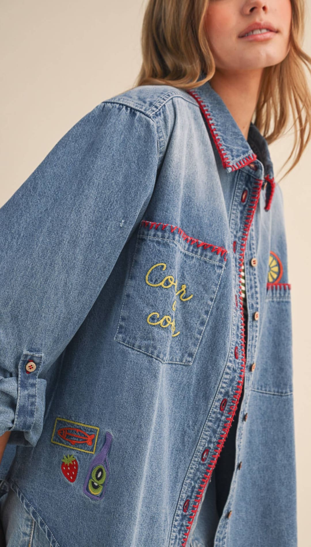 Light-wash denim jacket adorned with colorful embroidered patches and red-stitched details.