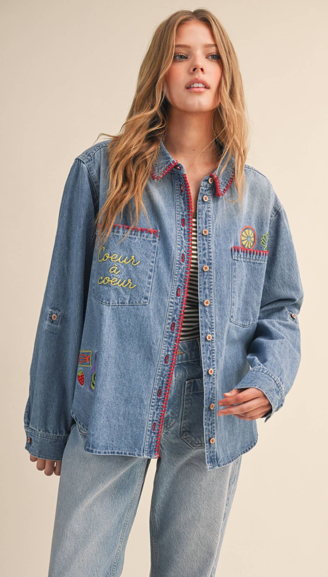 Light-wash denim jacket with colorful embroidered patches and red-trimmed pockets.