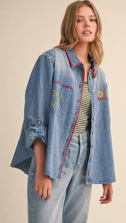 Light-wash denim shirt with red and yellow embroidery on the collar, pockets, and sleeves.