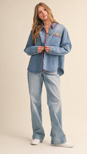 Light-wash denim button-up shirt with colorful embroidered floral and text details along the collar, placket, and chest pocket.