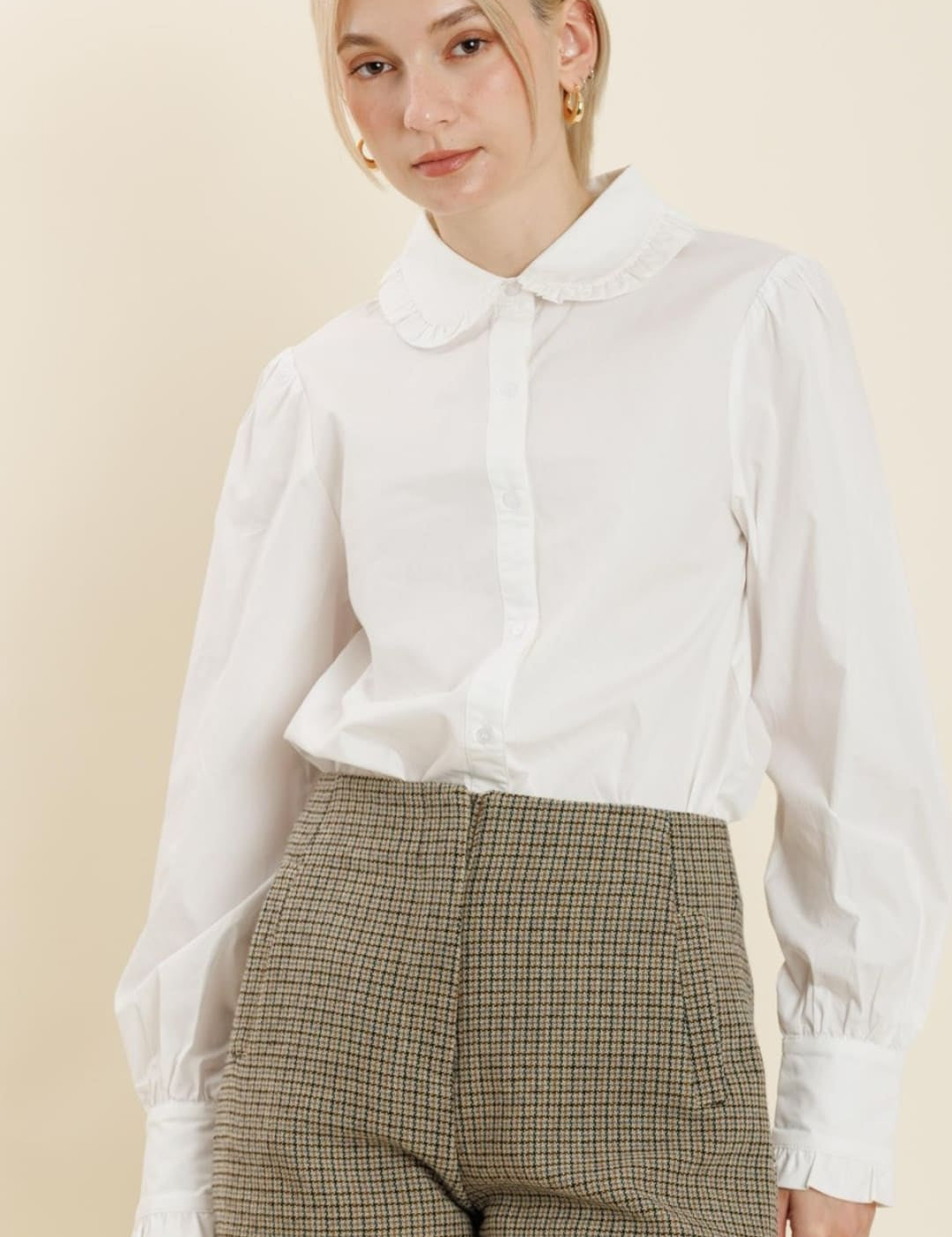 A white collared shirt with puffy sleeves and olive green plaid shorts.
