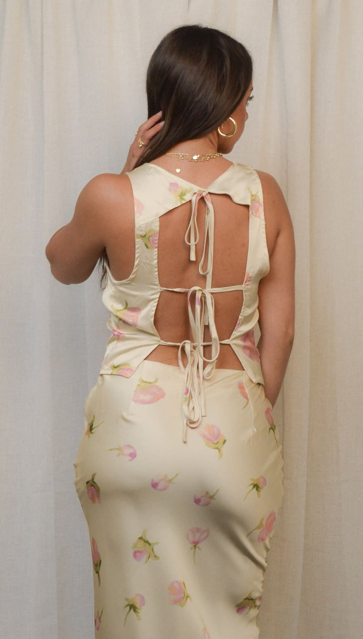 A light yellow sleeveless dress with pink floral patterns and a tie-back design.