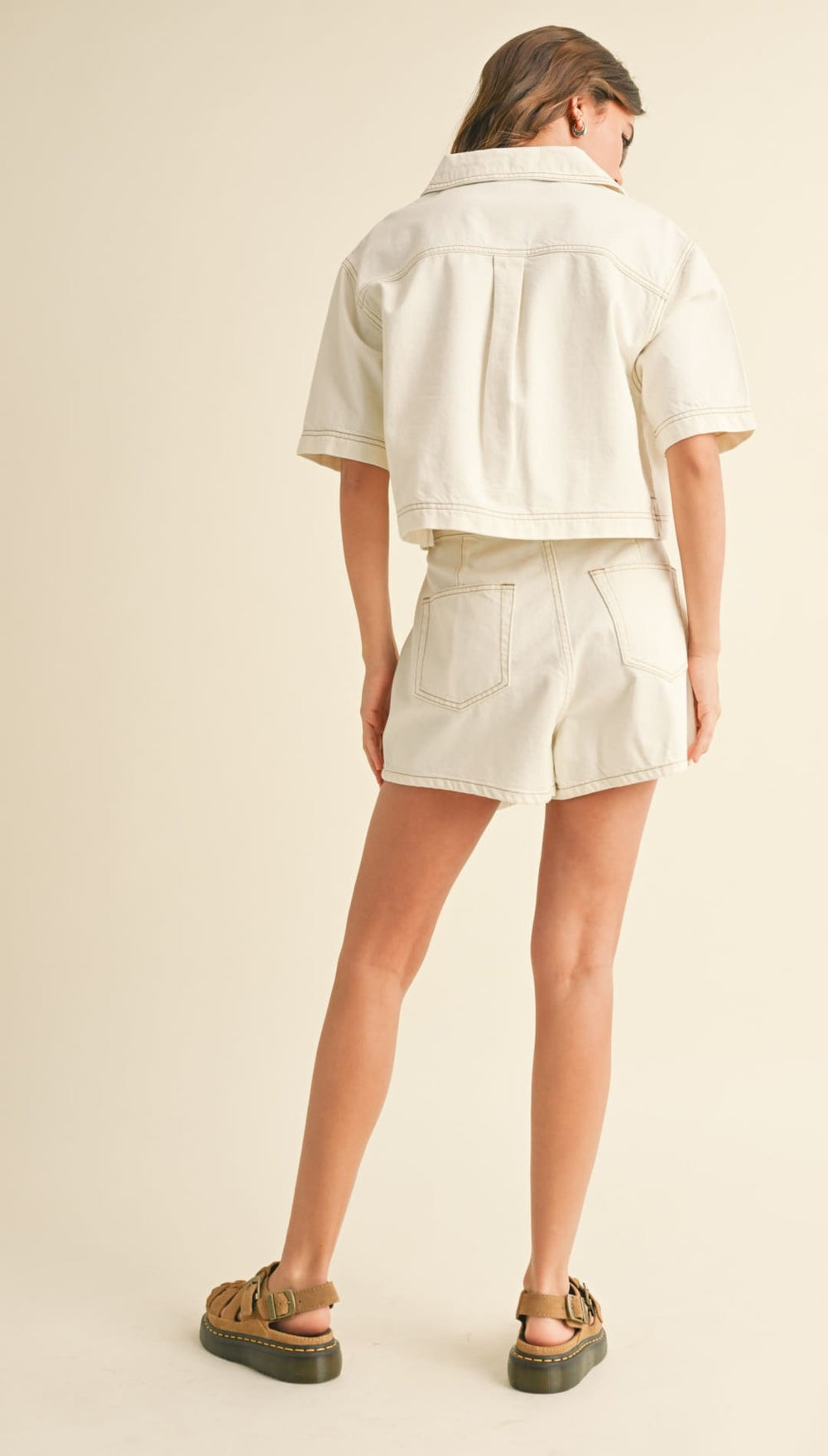 Woman wearing a matching cream-colored short-sleeved shirt and shorts with brown sandals.