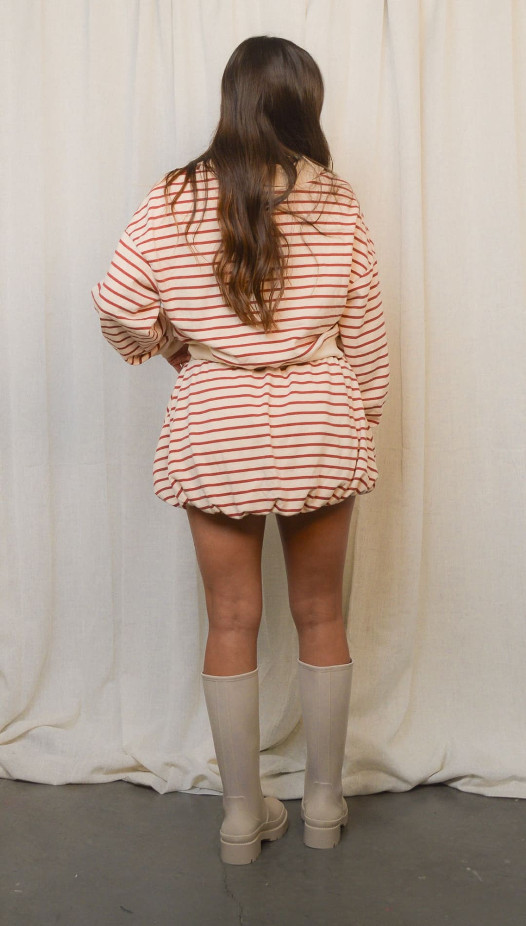 A woman’s striped beige and red romper with a tie waist and light-colored knee-high boots.