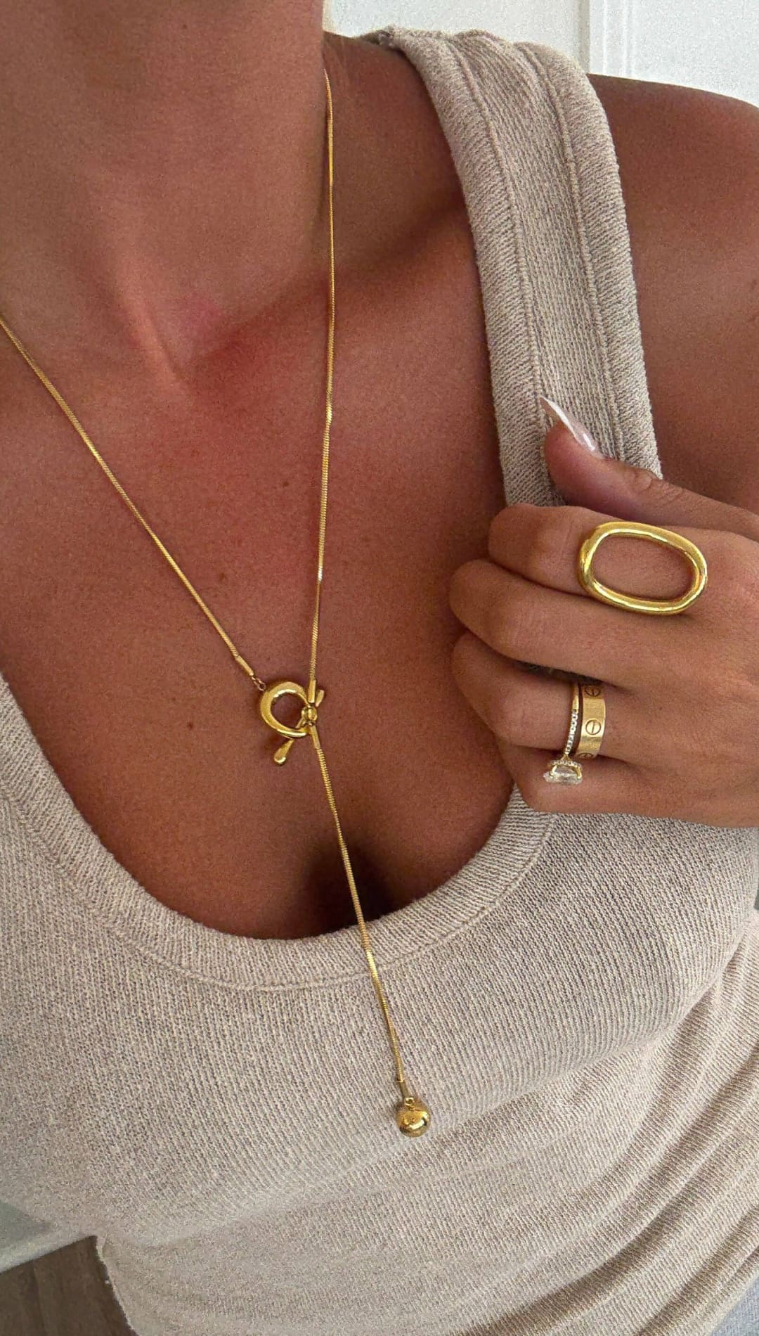 Gold-toned necklace with a delicate chain, featuring an elegant knot pendant and a small dangling bead.
