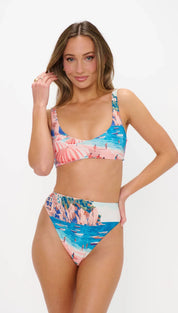 A vibrant, high-waisted bikini set featuring a tropical beach scene with pink and blue hues on stretchy fabric.