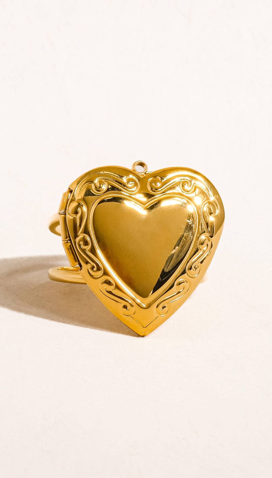 Gold heart-shaped locket with intricate scrollwork detailing and a polished metallic finish.