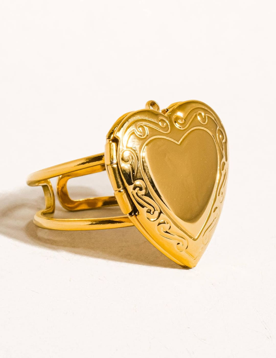 Gold heart-shaped locket ring with intricate scrollwork detailing.