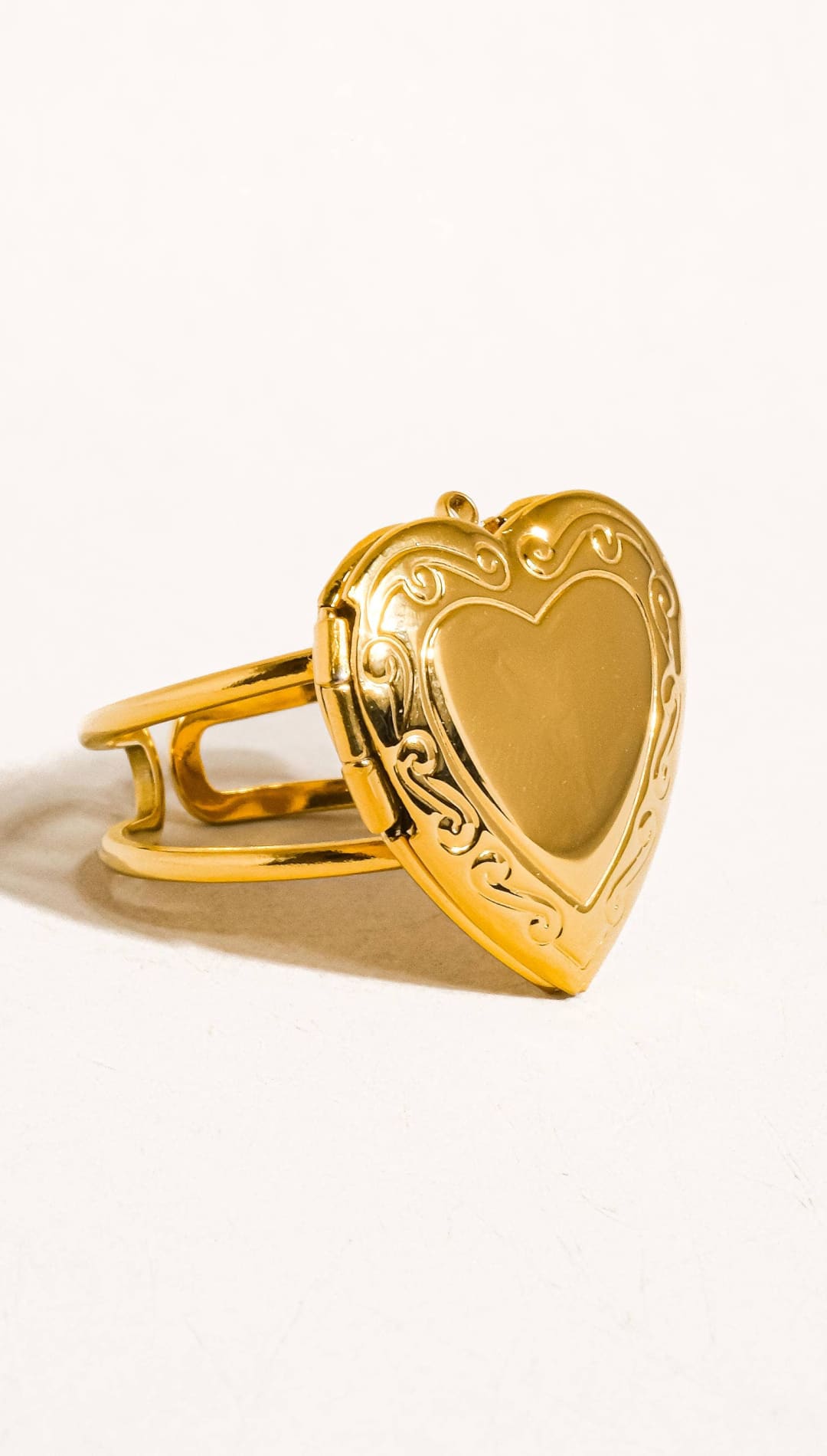 Gold heart-shaped locket ring with intricate scrollwork detailing.