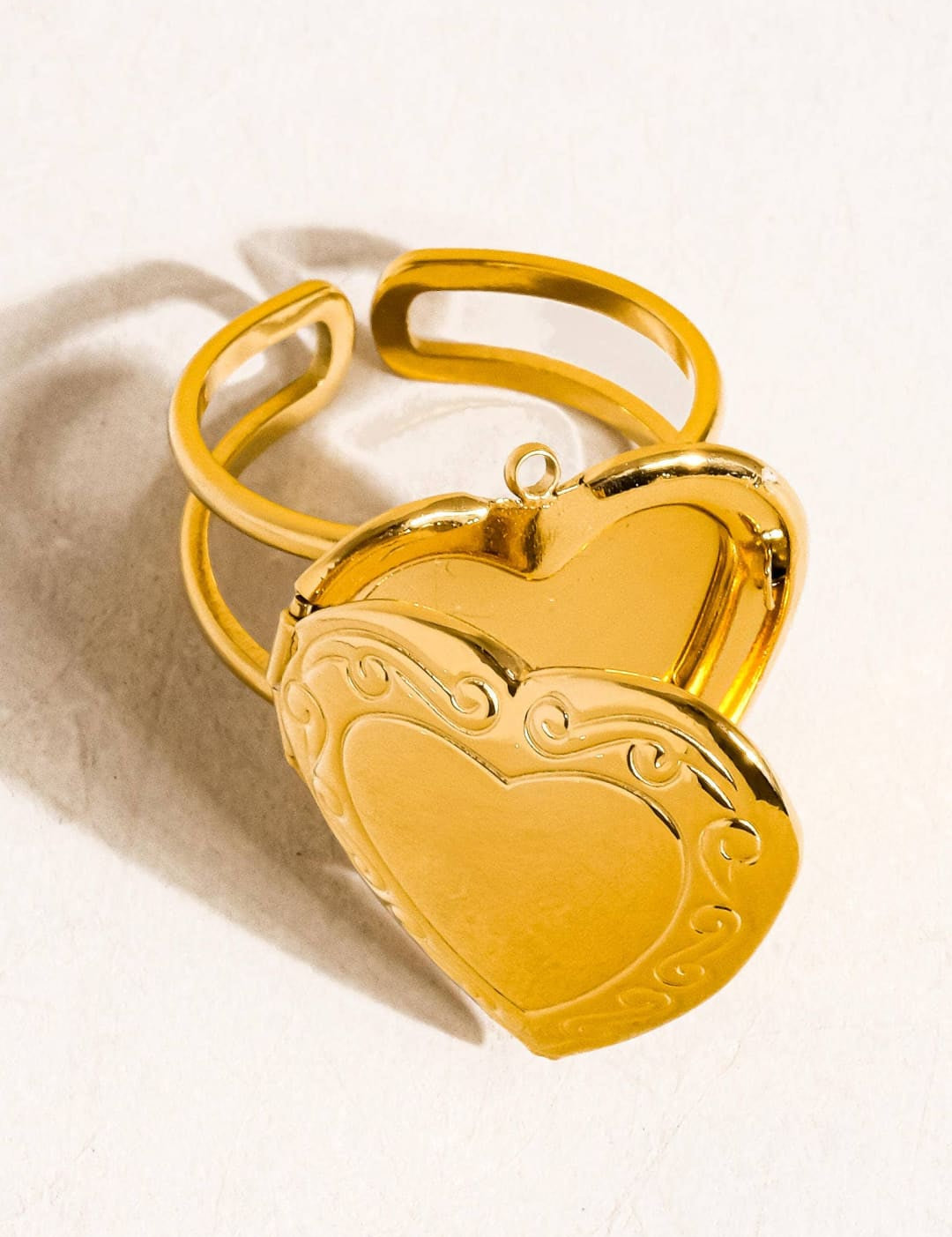 Gold-toned heart-shaped locket ring with ornate scrollwork detailing and a hinged design.