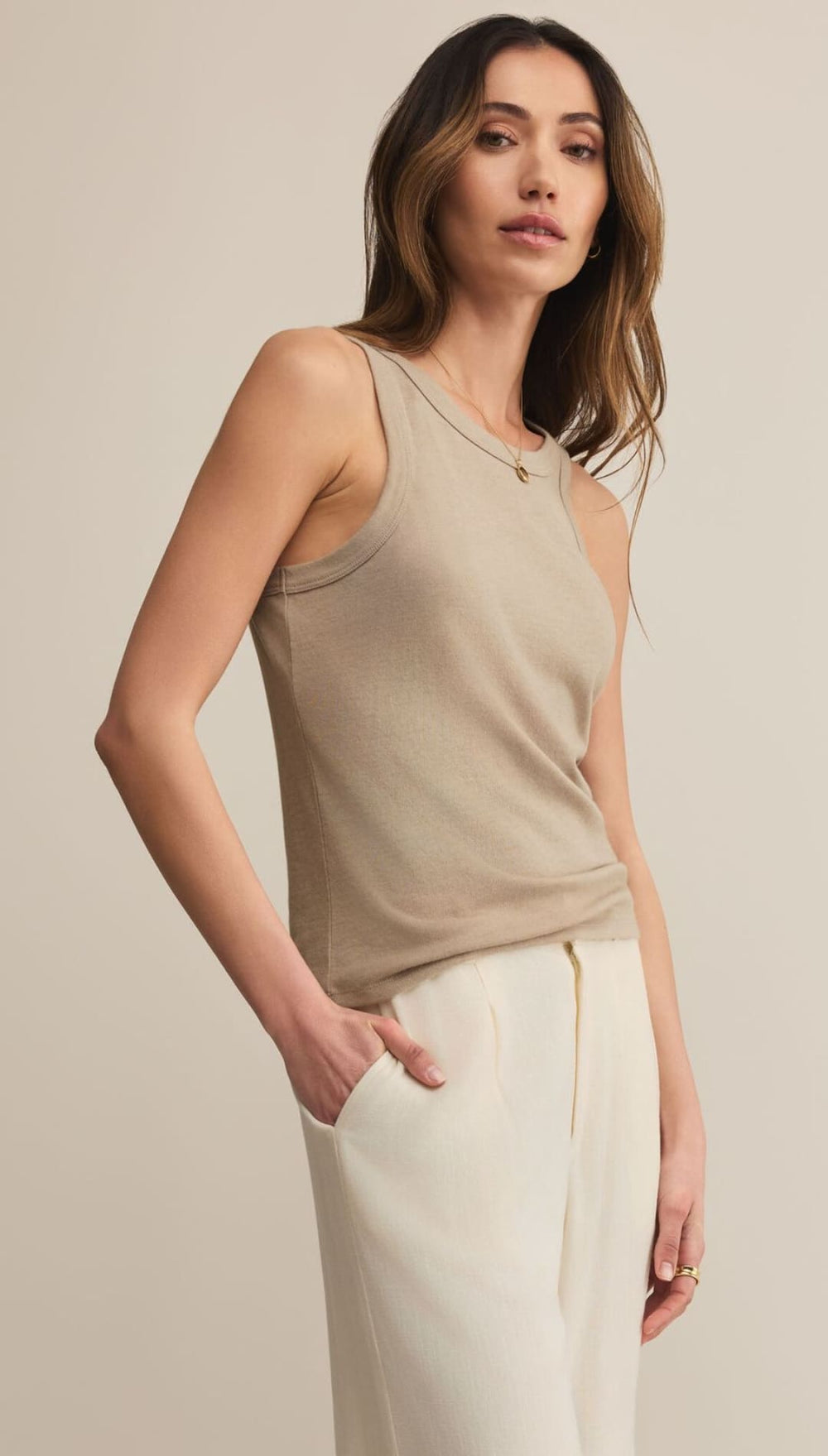 A woman wearing a beige ribbed tank top and off-white trousers.