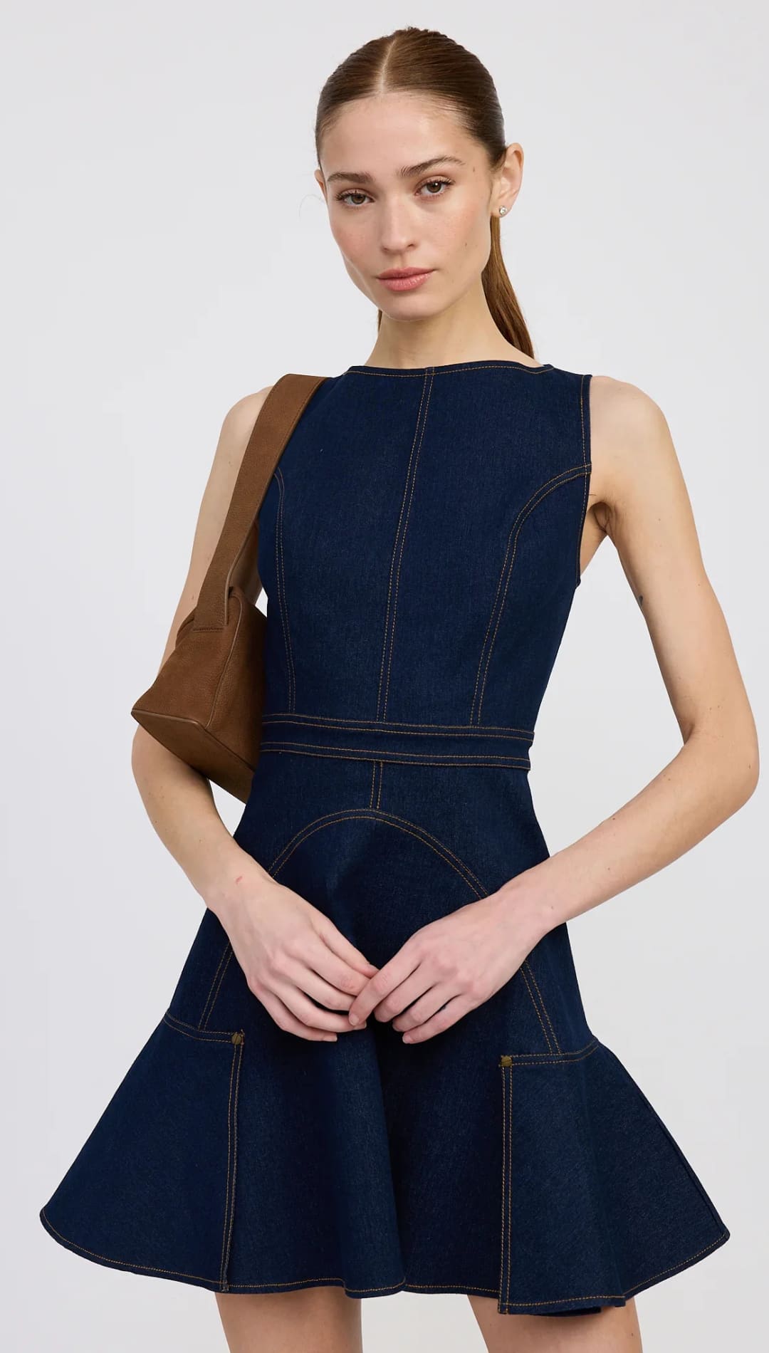 Sleeveless dark blue denim mini dress with visible tan stitching and a flared hem.