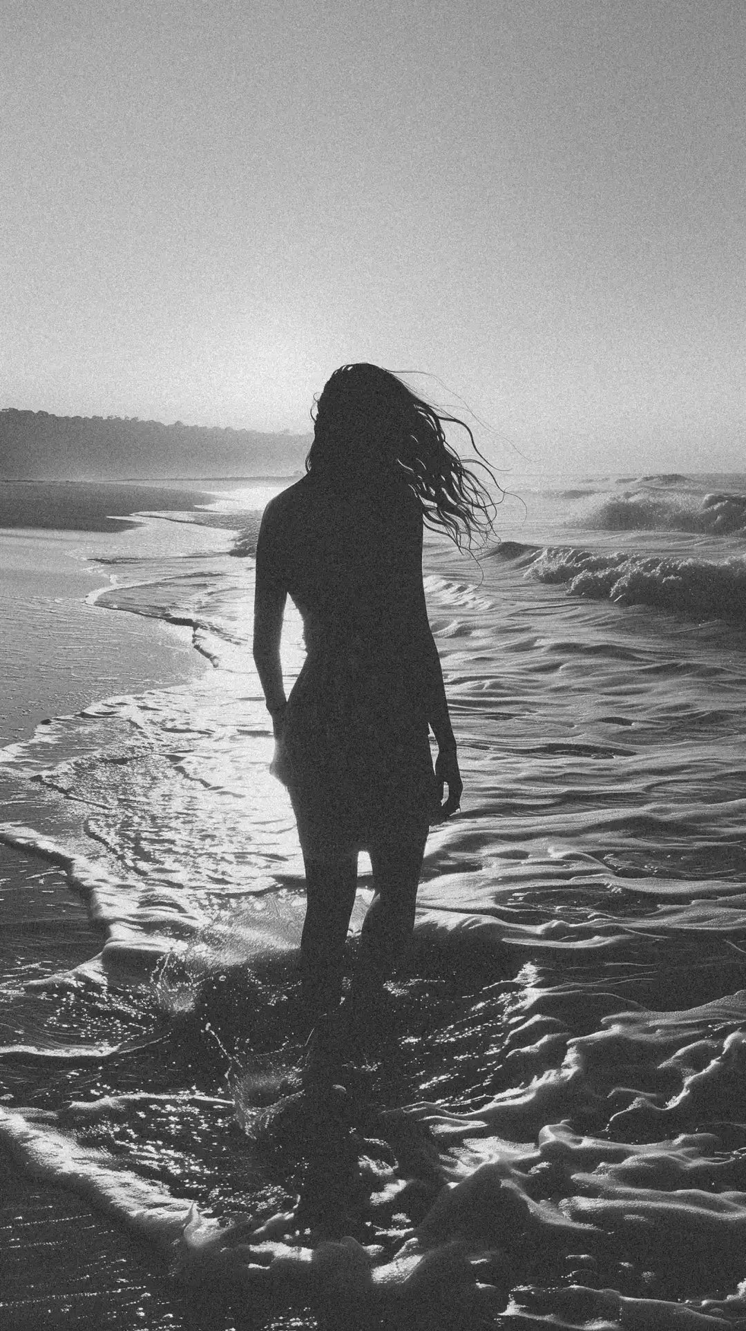 A silhouetted figure standing in ocean waves with windswept hair.