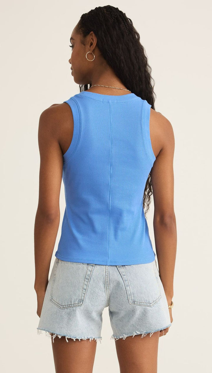 Woman in a blue ribbed tank top and denim shorts.
