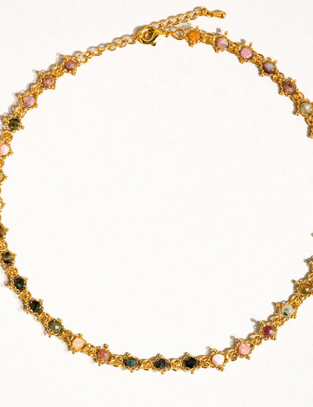 A delicate gold-toned necklace featuring a series of colorful, faceted gemstones in shades of pink, green, and black set within intricate star-shaped metalwork.
