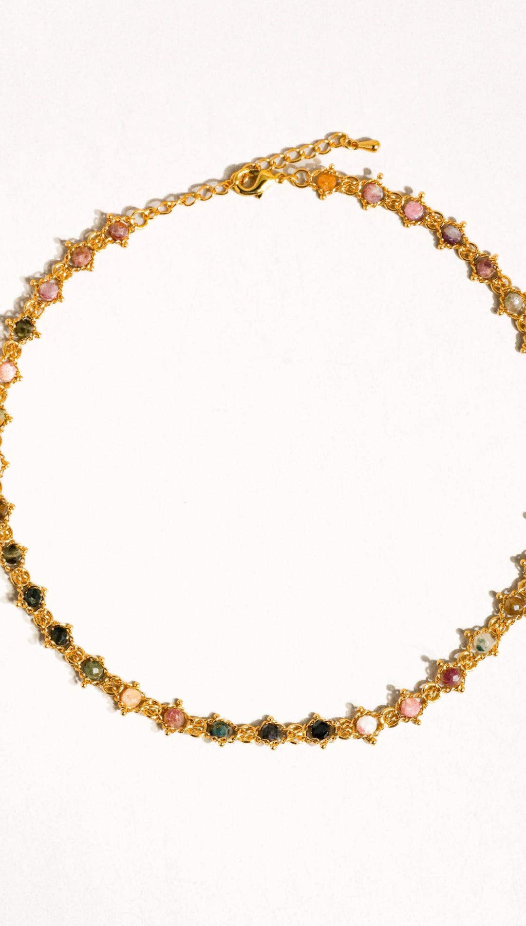 A delicate gold-toned necklace featuring a series of colorful, faceted gemstones in shades of pink, green, and black set within intricate star-shaped metalwork.