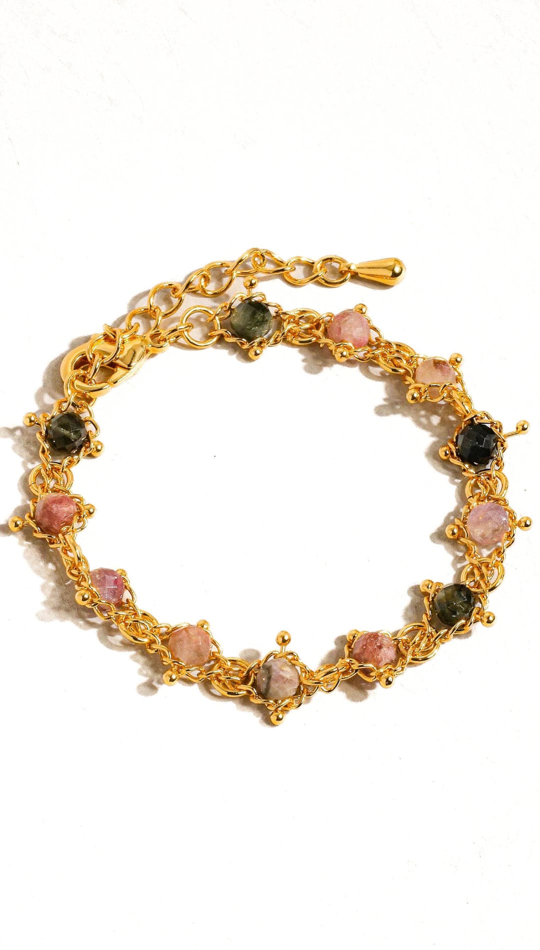 Gold-toned bracelet featuring a chain design with alternating pink and dark green gemstones set in intricate metalwork.