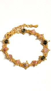 Gold-toned bracelet featuring a chain design with alternating pink and dark green gemstones set in intricate metalwork.
