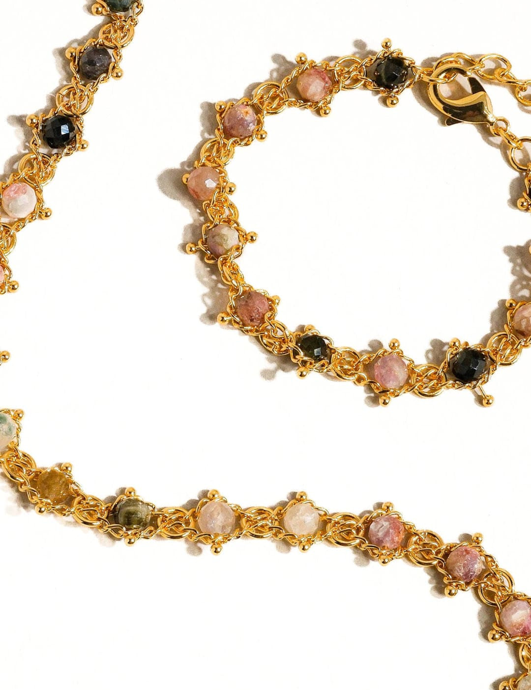 Gold-toned jewelry set featuring a necklace and bracelet adorned with colorful, faceted gemstones in shades of pink, green, black, and white.