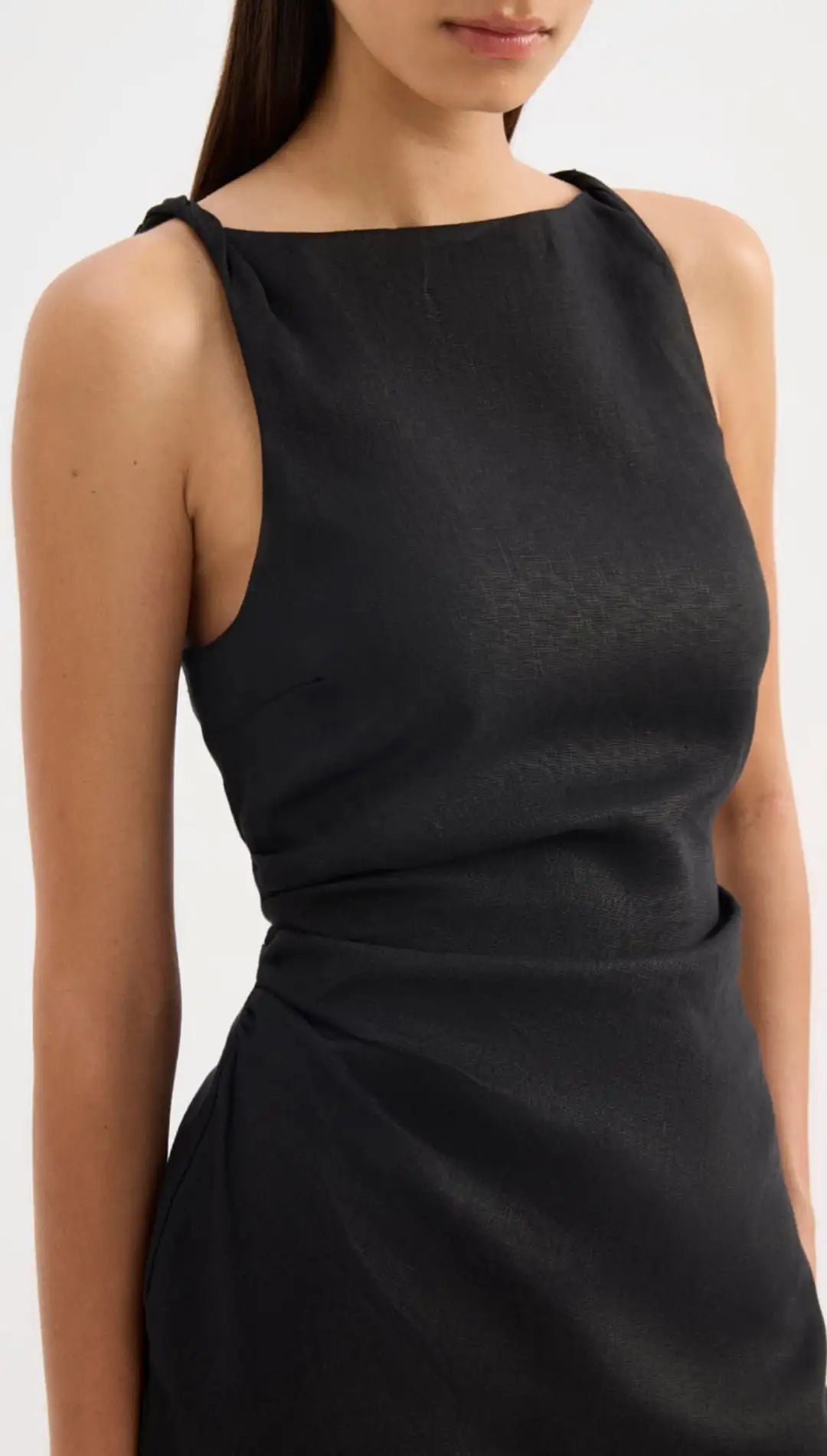 Black sleeveless dress with a draped waistline and soft, flowing fabric.
