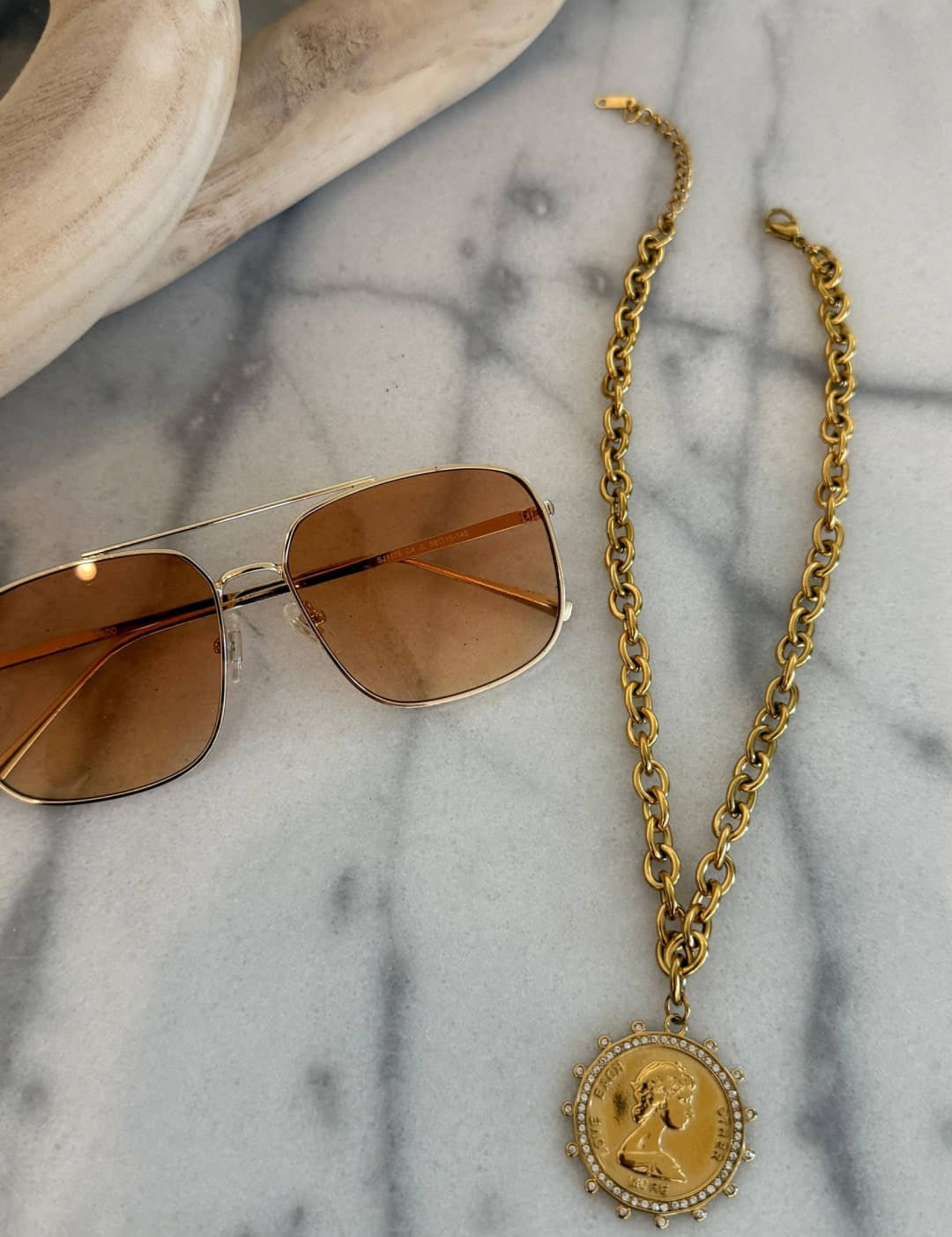 Gold chain necklace with a circular pendant featuring an engraved profile and surrounded by small stones.