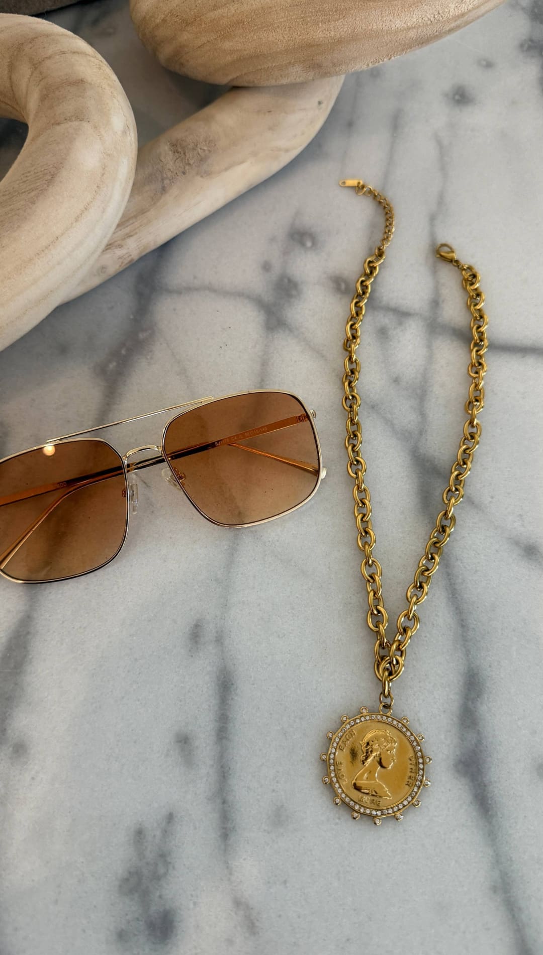 Gold chain necklace with a circular pendant featuring an engraved profile and surrounded by small stones.