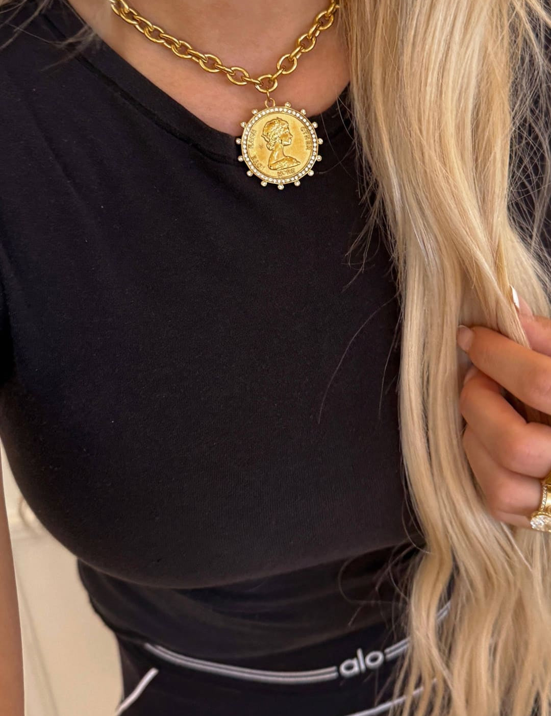 Gold chain necklace with a circular medallion pendant featuring an engraved portrait and surrounded by small clear stones.