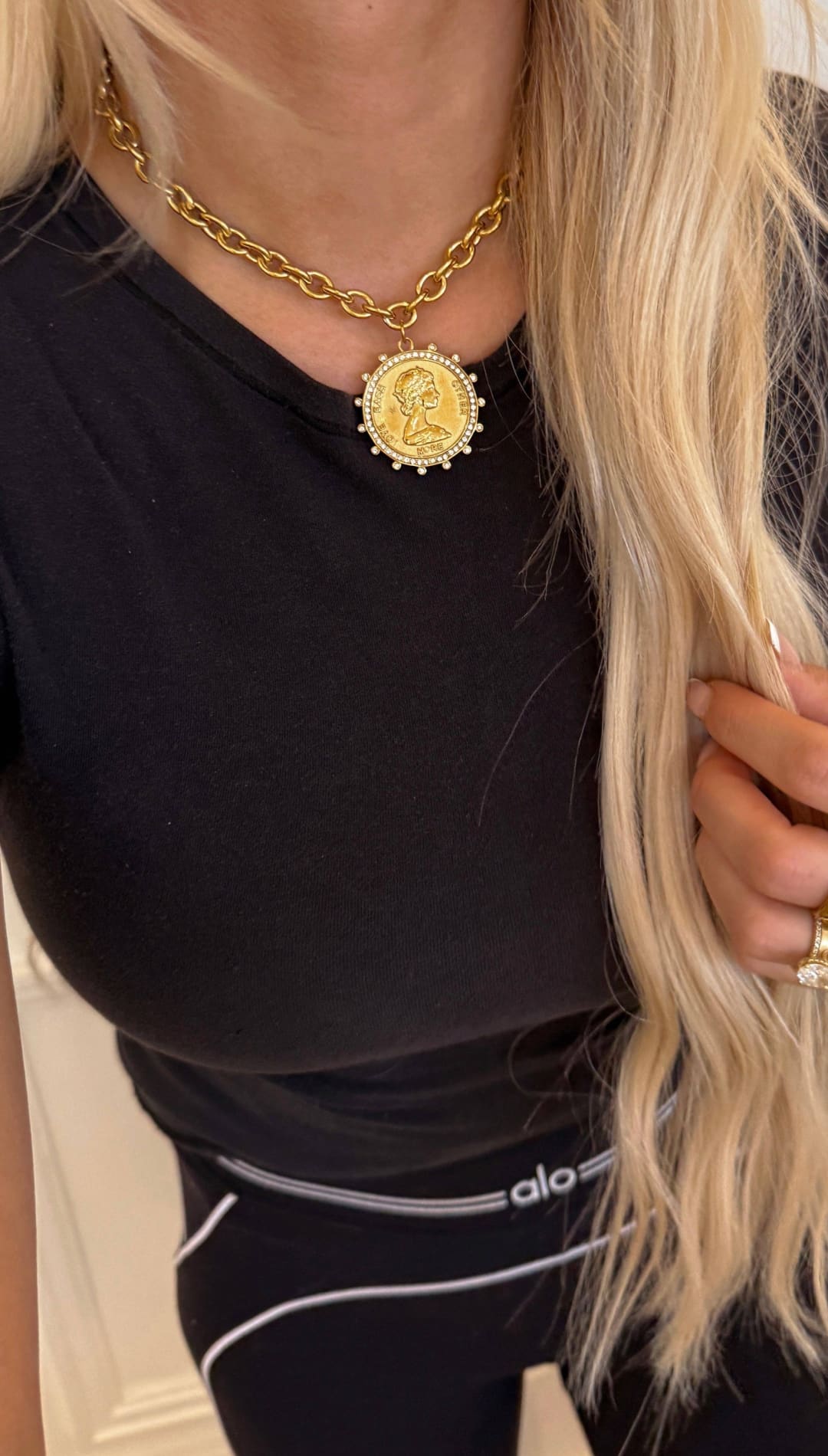 Gold chain necklace with a circular medallion pendant featuring an engraved portrait and surrounded by small clear stones.