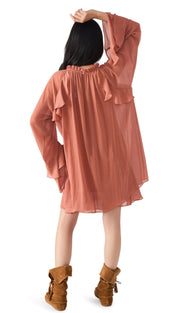 A young girl wearing a long-sleeved, ruffled, salmon-colored tunic dress and brown moccasin boots.