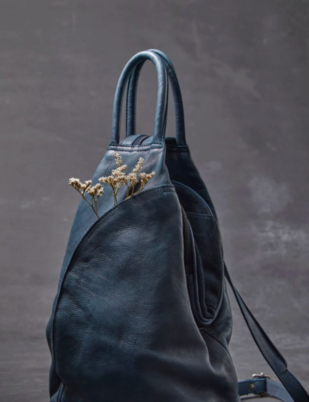 Dark blue leather backpack with a soft, slightly wrinkled texture and minimalist design.