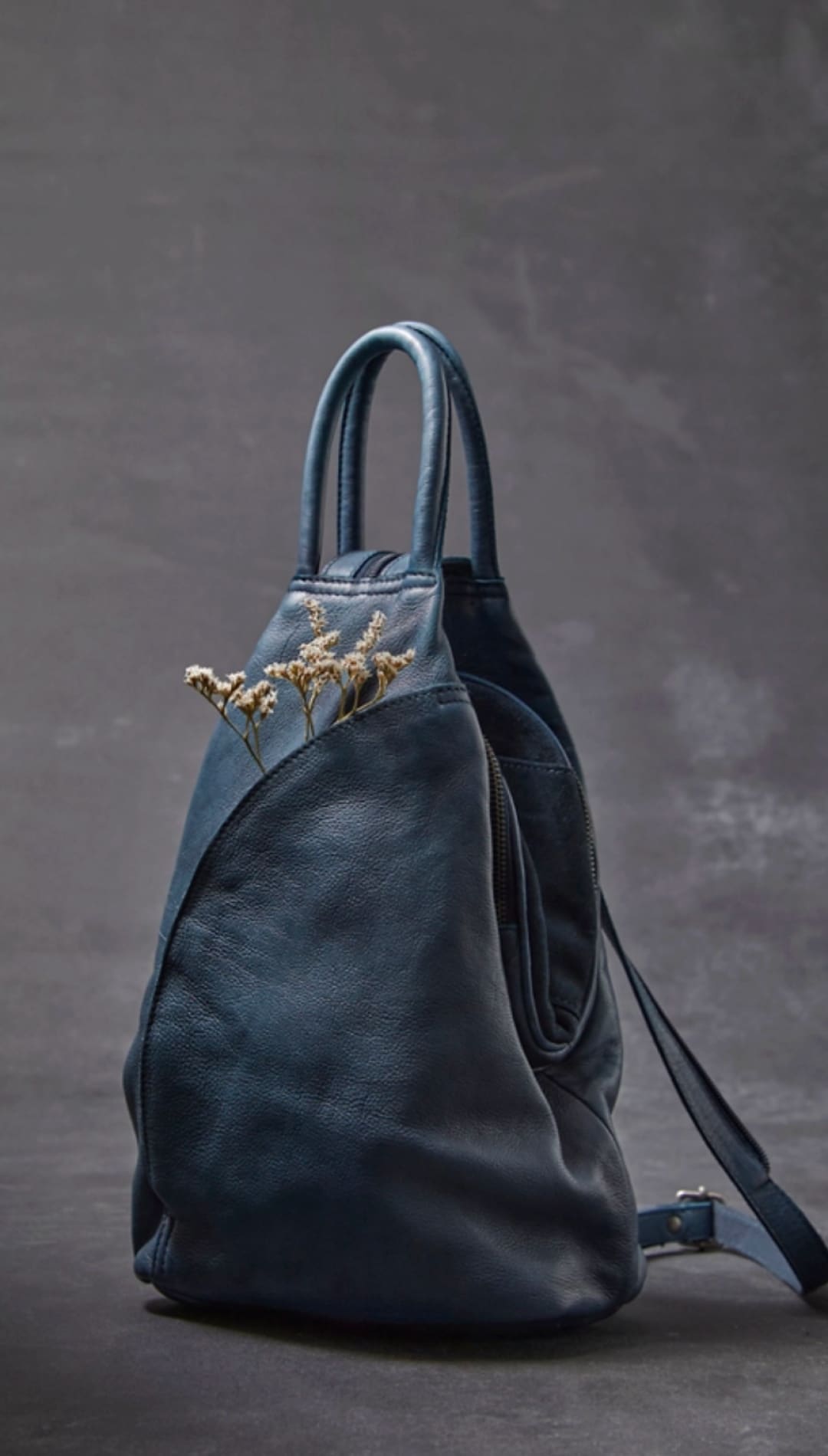 Dark blue leather backpack with a soft, slightly wrinkled texture and minimalist design.