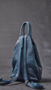 A soft, dusty blue leather backpack with a minimalist design and dual zippers.