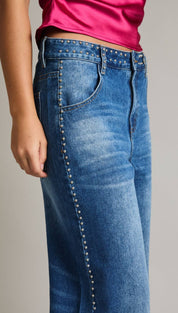 Blue denim jeans with silver studs along the side seam.