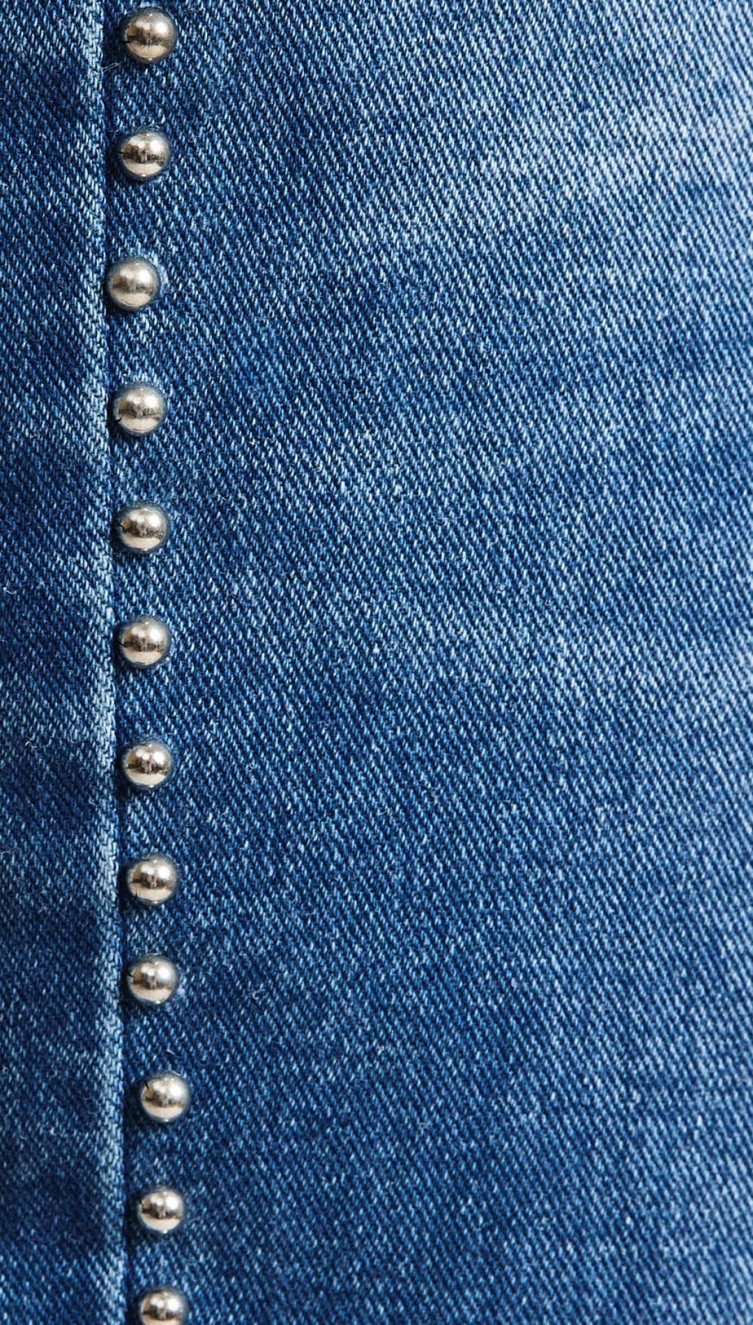 Blue denim fabric with a vertical line of silver-toned metal studs.