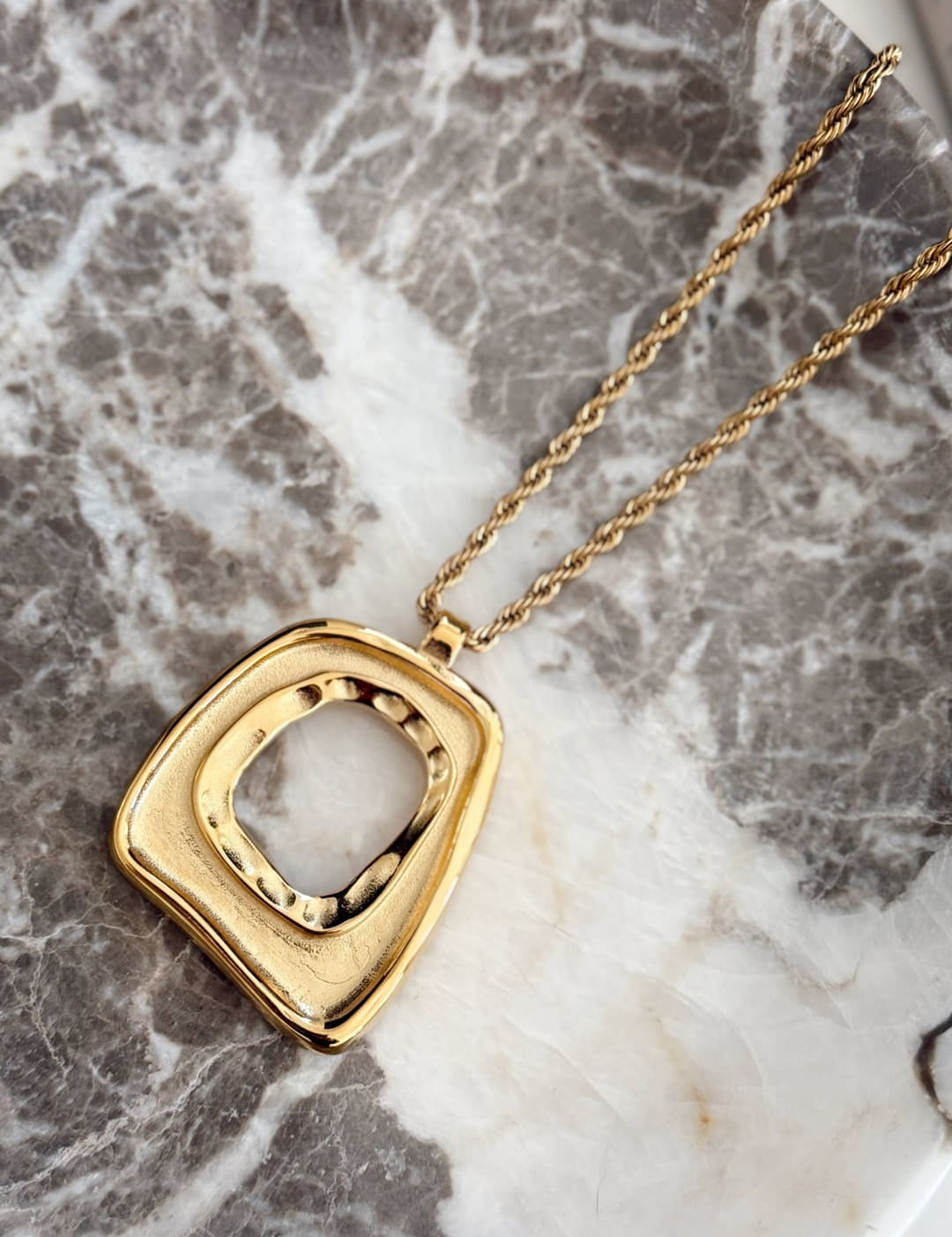 Gold-toned geometric pendant necklace with a textured, square-shaped frame and an open center.