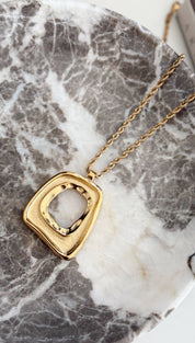 Gold-toned geometric pendant necklace with a textured, square-shaped frame and an open center.