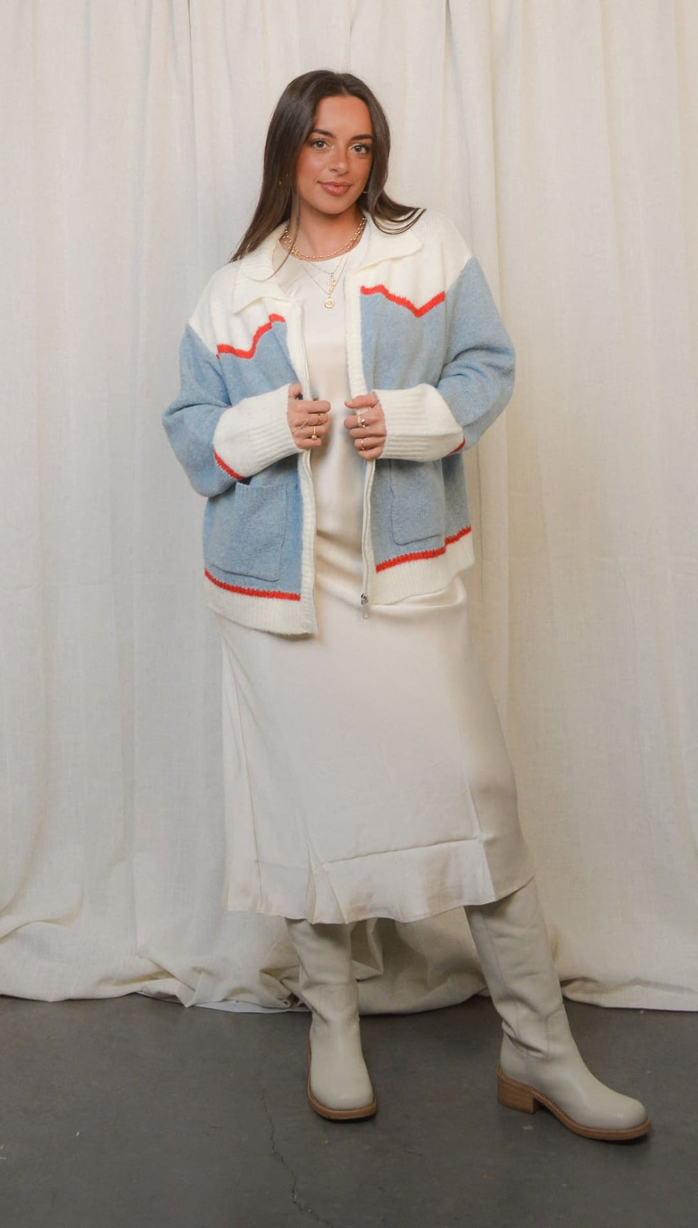 A light blue and white color block jacket with red trim, worn over a white dress and knee-high boots.