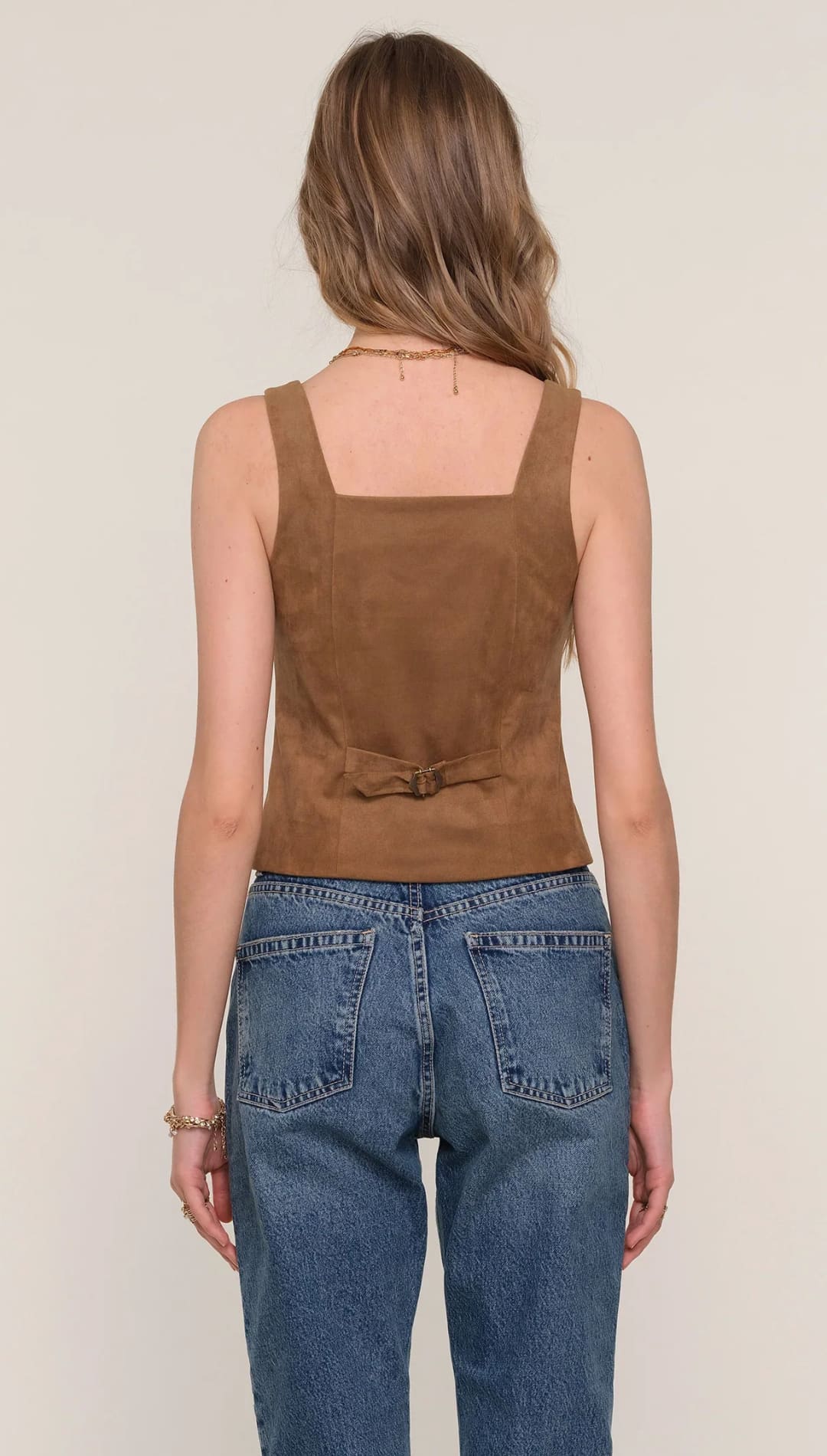 A woman’s brown suede sleeveless tank top with a square neckline, paired with blue denim jeans.