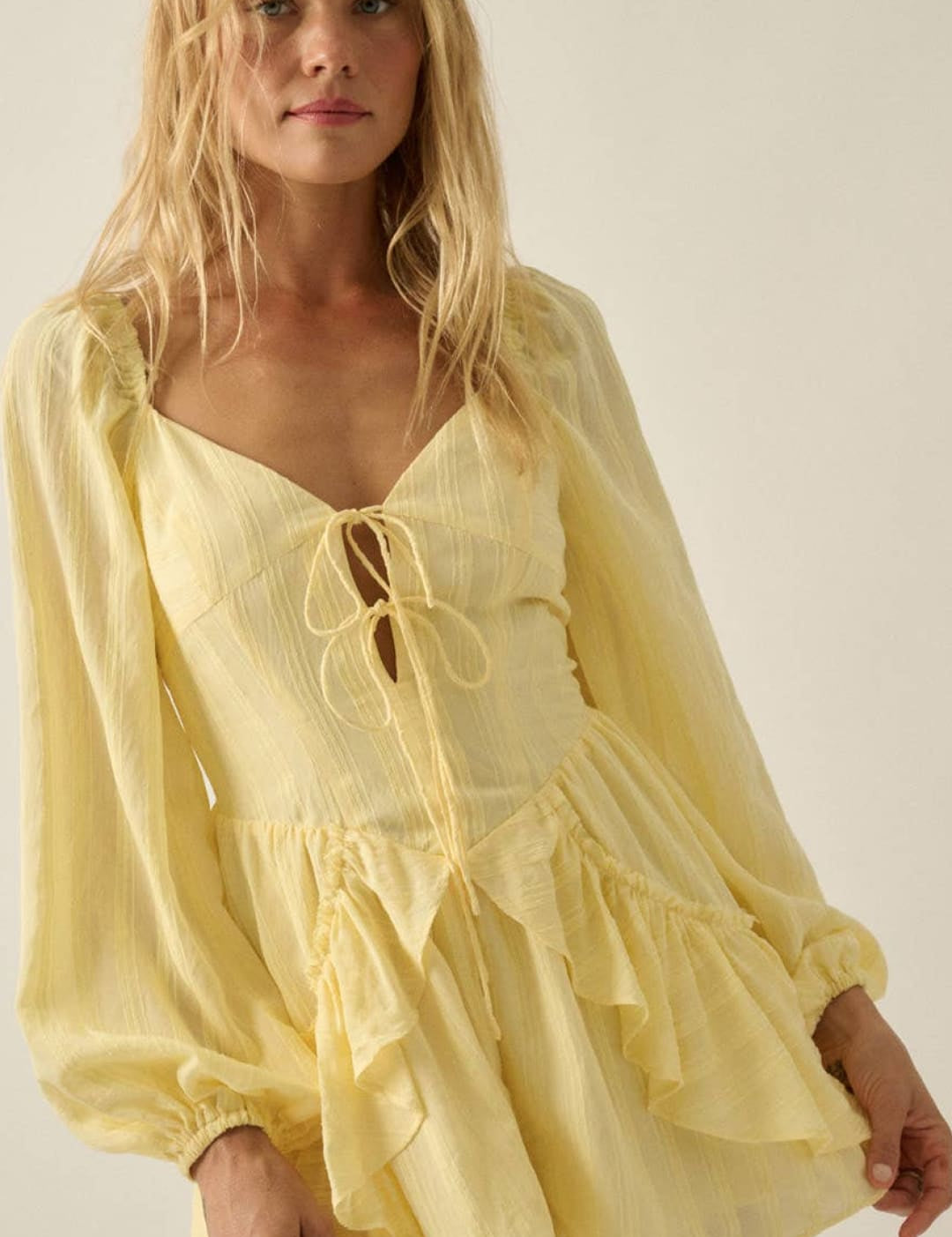 A soft yellow, long-sleeved romper with a lace-up front and ruffled hem.