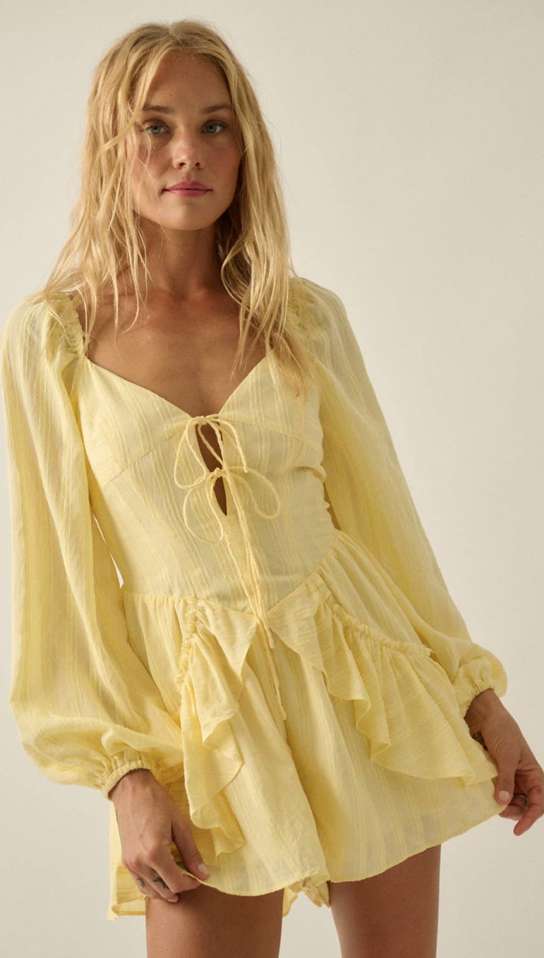 A soft yellow, long-sleeved romper with a lace-up front and ruffled hem.