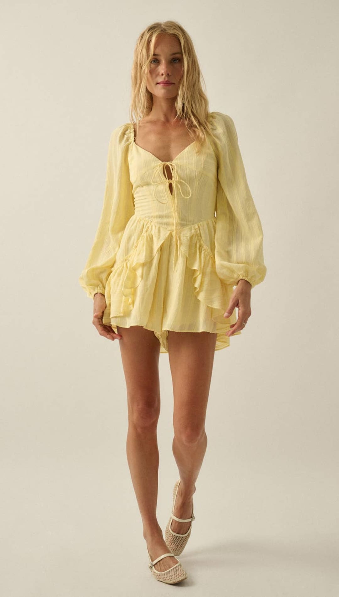 A soft yellow, long-sleeved mini dress with a ruffled hem and lace-up front.
