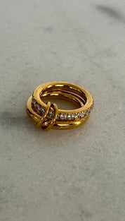 Gold-toned ring with a layered, intertwined design and a band of sparkling clear stones.