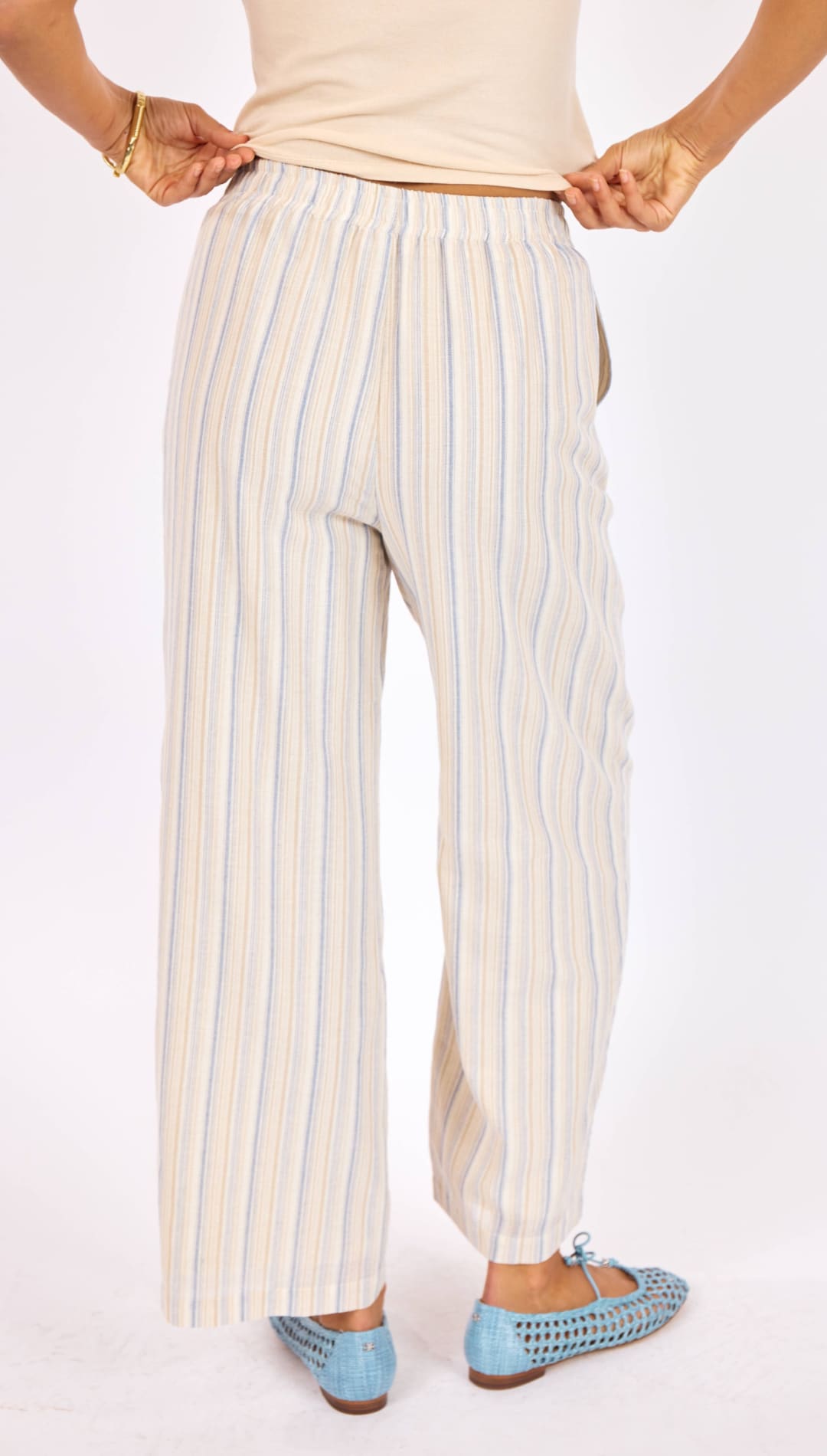Cream-colored wide-leg trousers with thin vertical stripes in light blue and beige, made of a lightweight woven fabric.